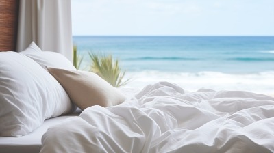 Chambre apaisante avec lit devant fenêtre, vue sur plage ensoleillée et océan.